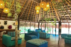 A spacious room with a high thatched ceiling, multiple hanging light fixtures, and a large window offering a view of greenery outside. - Collection O EcoVergel Hotel Boutique Spa in Tulum  (Tulum)