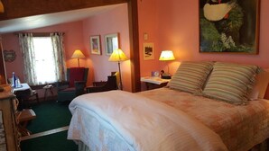 Een hotelkamer met een groot bed, twee bedlampen, een bureau met stoel, een raam met gordijnen en een schilderij aan de muur.