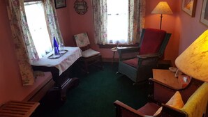 Een gezellige kamer met een groen tapijt, een tafel met een witte tafelkleed, twee stoelen, een lamp en bloemen gordijnen.