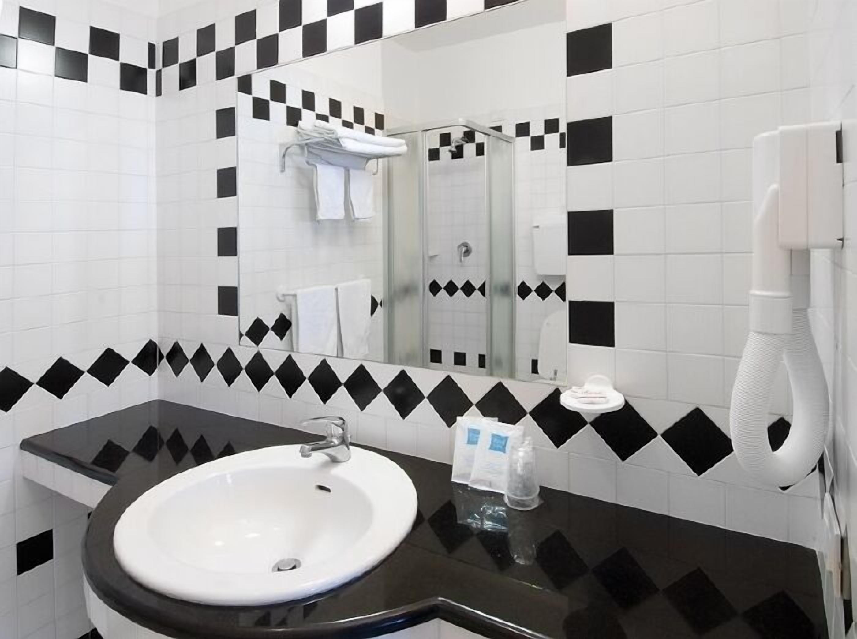 A bathroom with a white sink, black and white checkered tiles, a mirror, and a white towel rack.