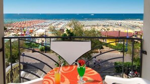 Un balcon avec une table et des chaises, donnant sur une plage parsemée de parasols et offrant une vue sur la mer.