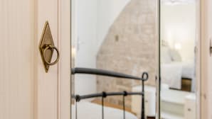 Une chambre avec un mur en pierre, un lit et un miroir qui reflète le lit et un mur blanc.