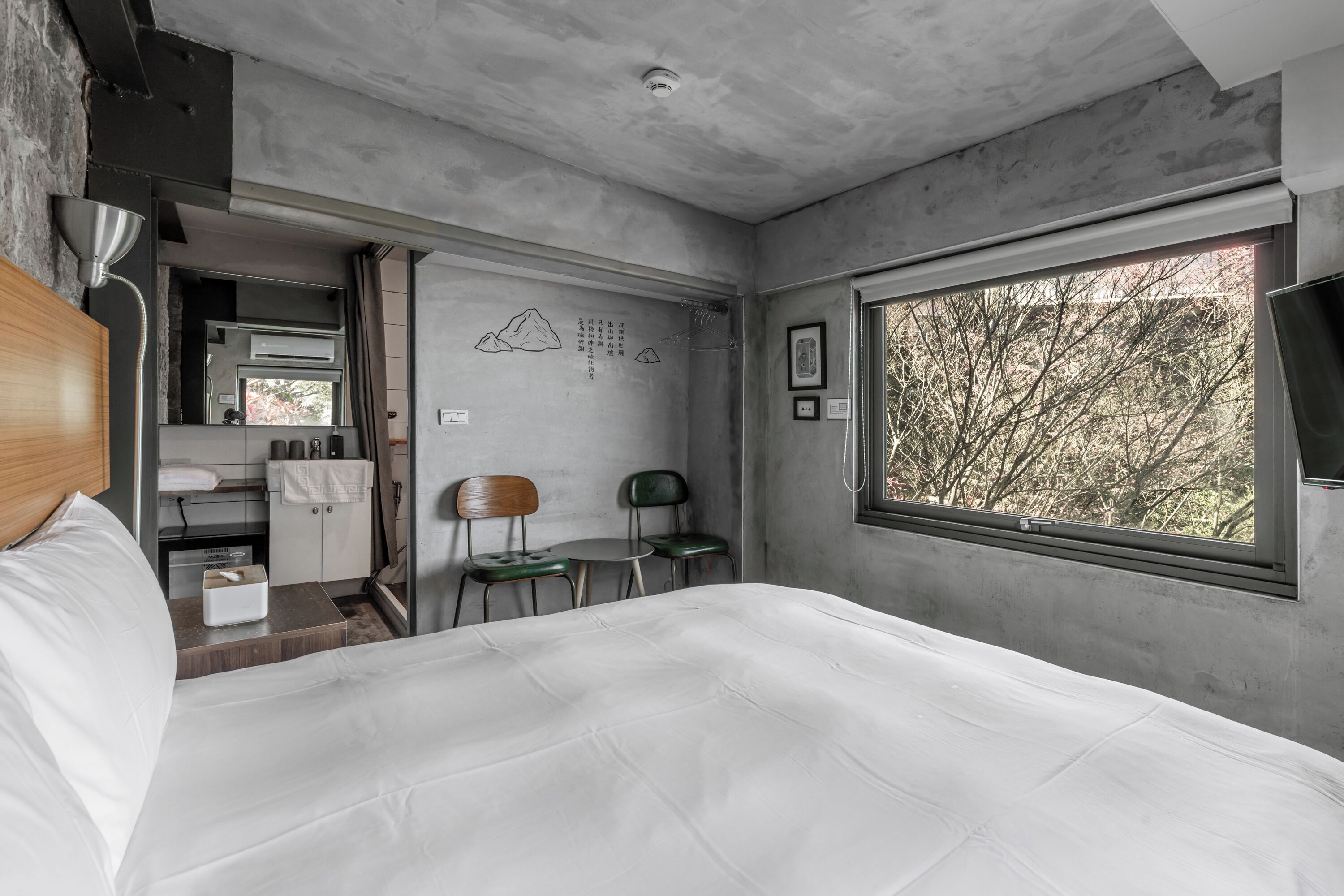 Habitación de hotel moderna con una cama grande, una kitchenette pequeña y una ventana con vistas a árboles.