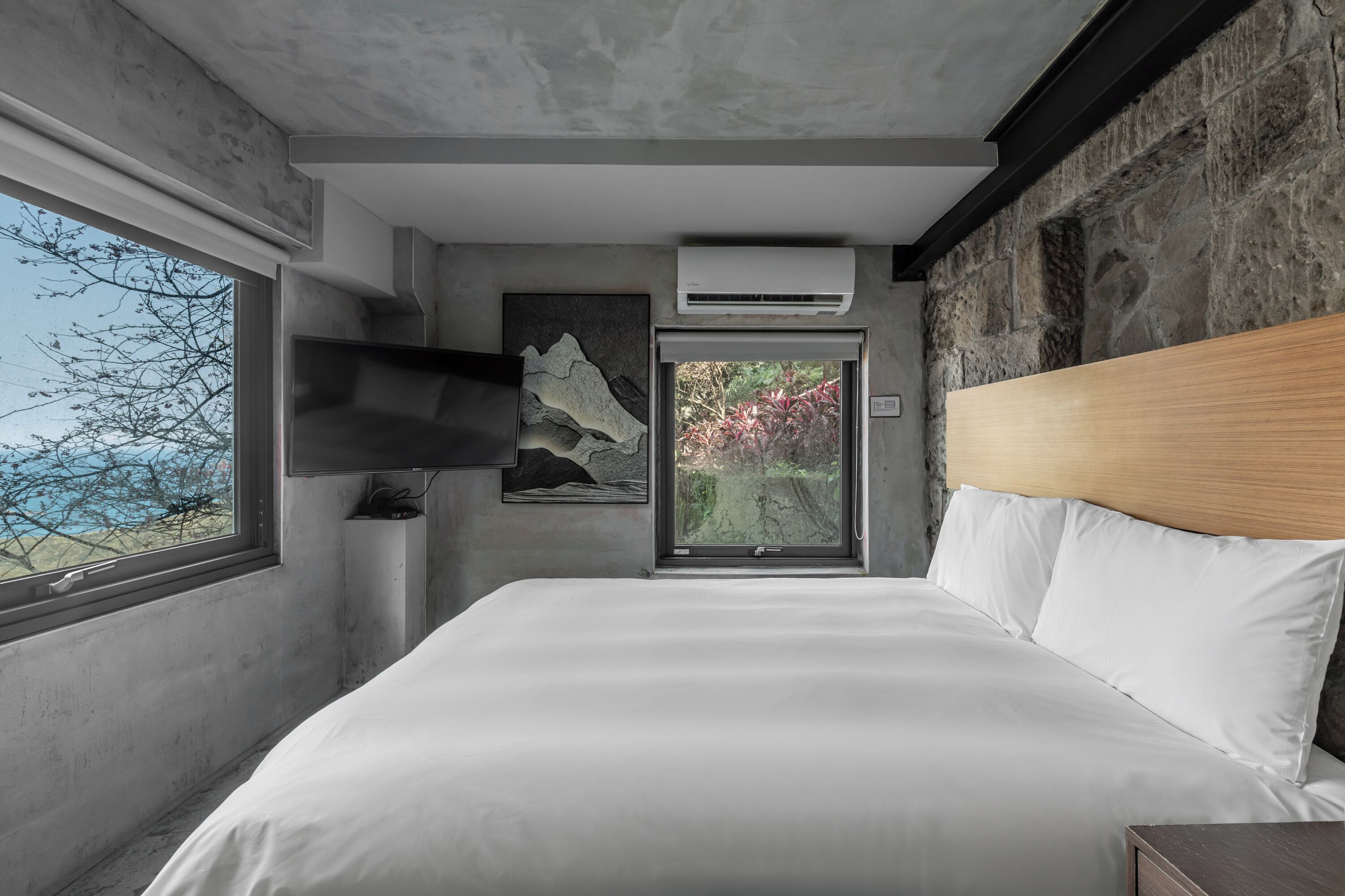 A modern bedroom with a large bed, a mounted TV, and a stone wall.