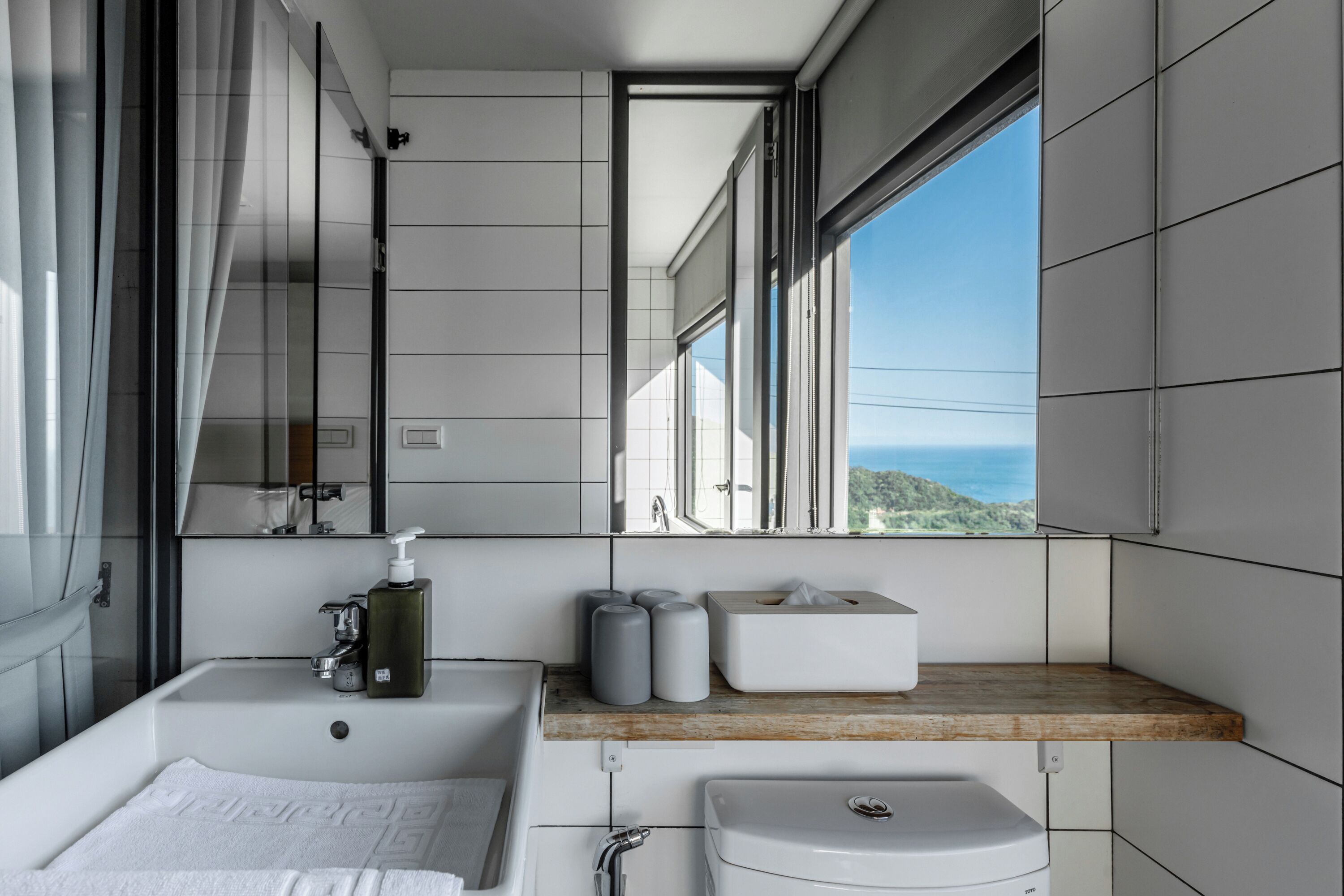 Une salle de bain moderne équipée d’une baignoire, d’un lavabo et d’une fenêtre donnant sur la mer.