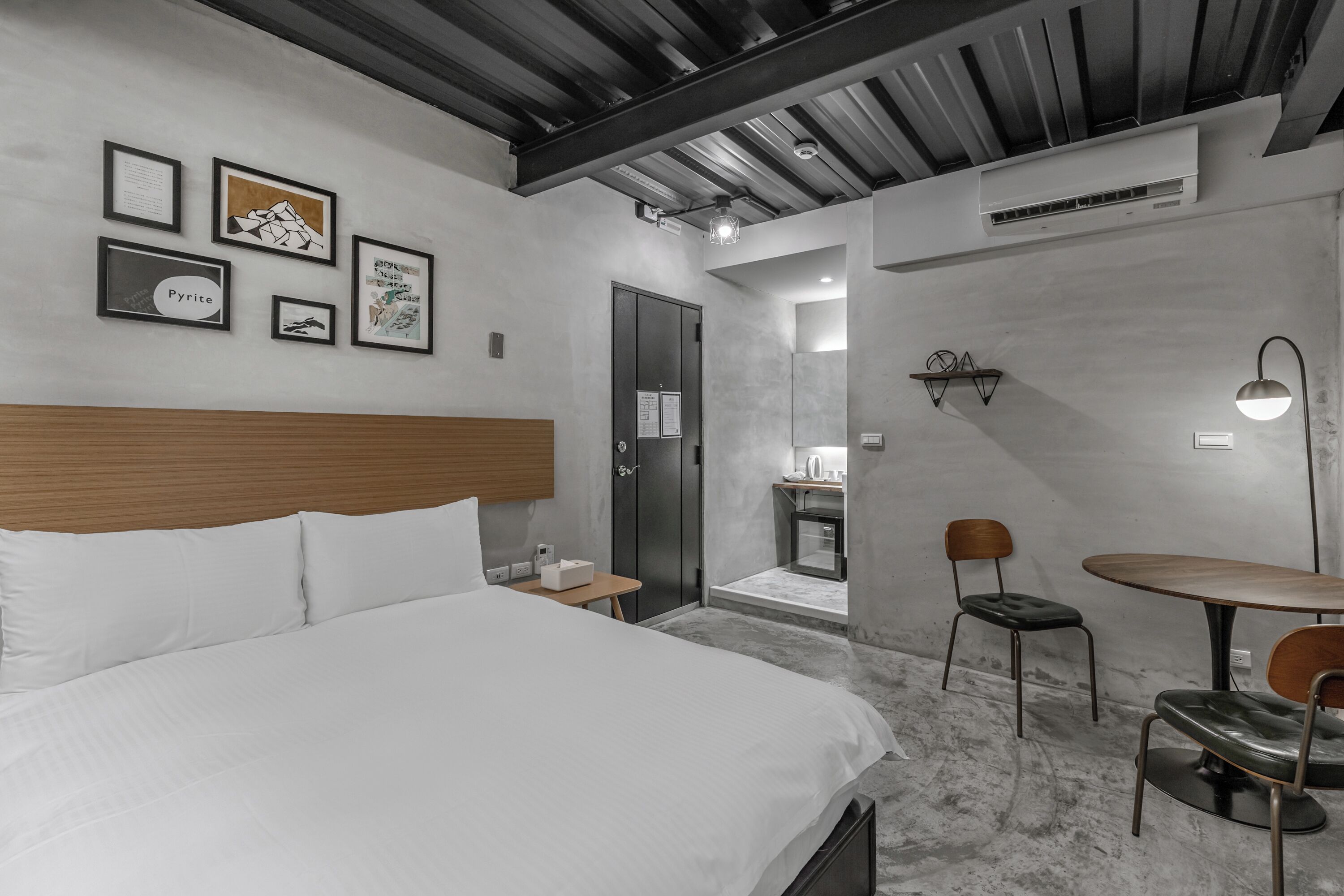 A modern hotel room with a large bed, a small table, two chairs, and artwork on the wall.