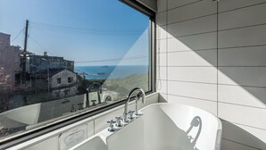 A modern bathroom with a large bathtub, a window with a view of the sea, and a tiled wall. - Jiufen The Ore Inn (New Taipei City)