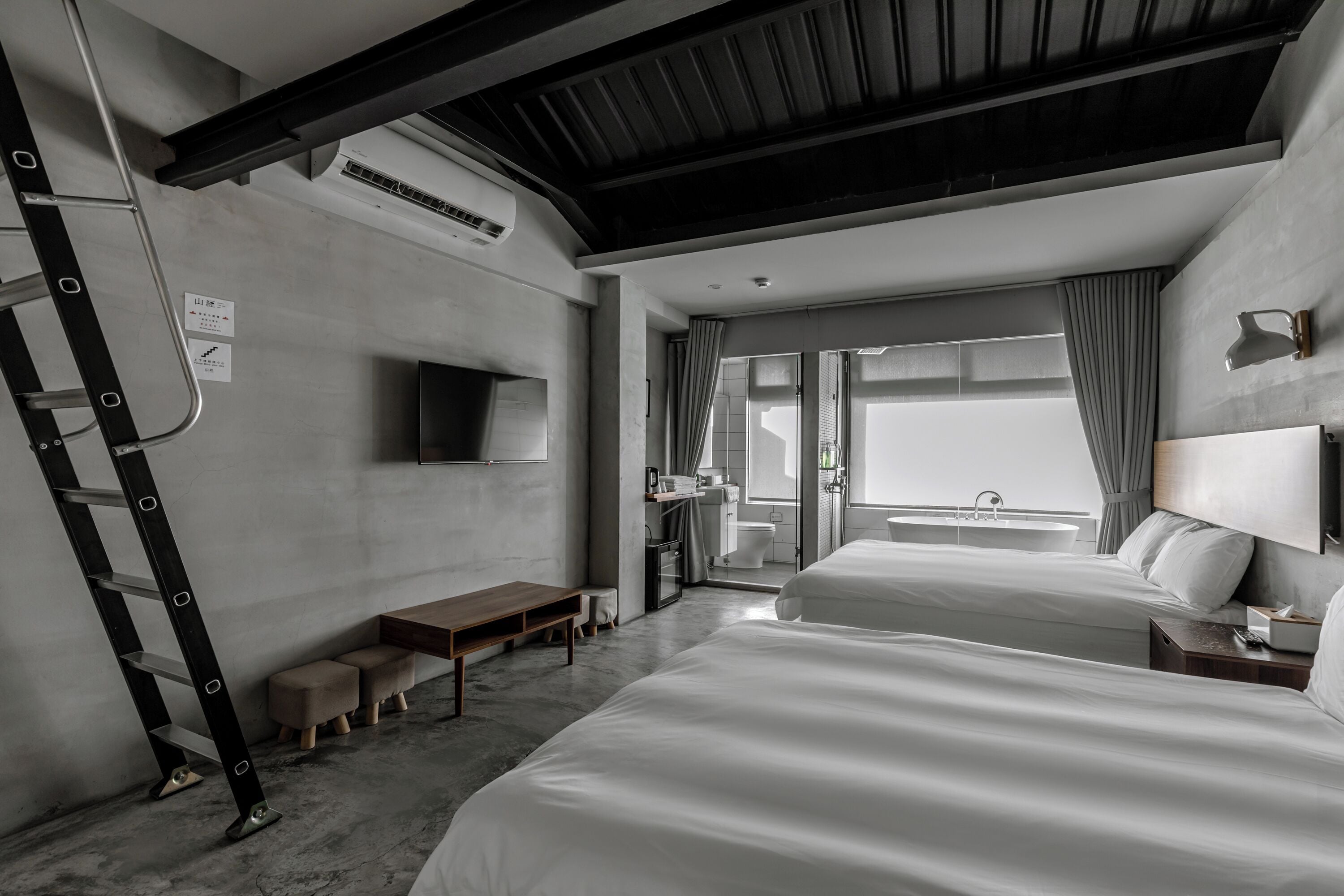 A modern hotel room with a large bed, a desk, a chair, and a TV mounted on the wall.
