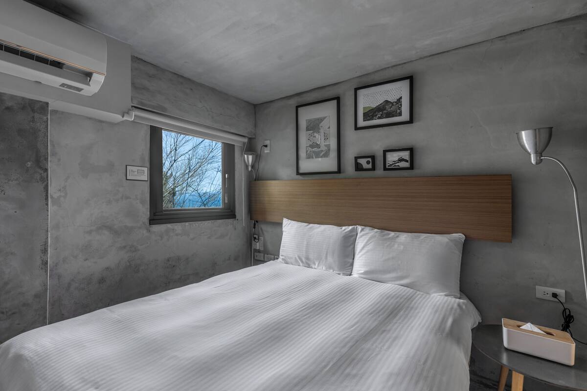 A modern bedroom with a large bed, a wooden headboard, a bedside table with a lamp, and framed pictures on the wall.