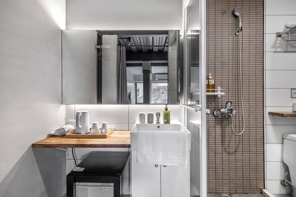 Un baño moderno con tocador de madera, un espejo grande, ducha con panel de control y un ventanal pequeño.
