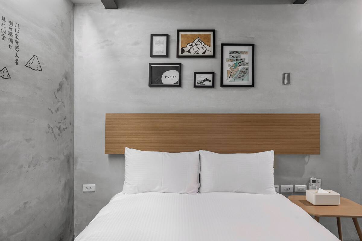 A modern hotel room with a wooden headboard, white bedding, and artwork on the wall.