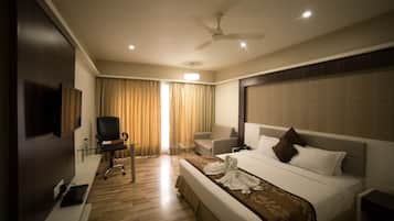 A hotel room with a bed, a desk, a chair, a television, and a ceiling fan.