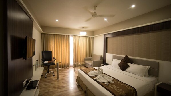 A hotel room with a bed, a desk, a chair, a television, and a ceiling fan.