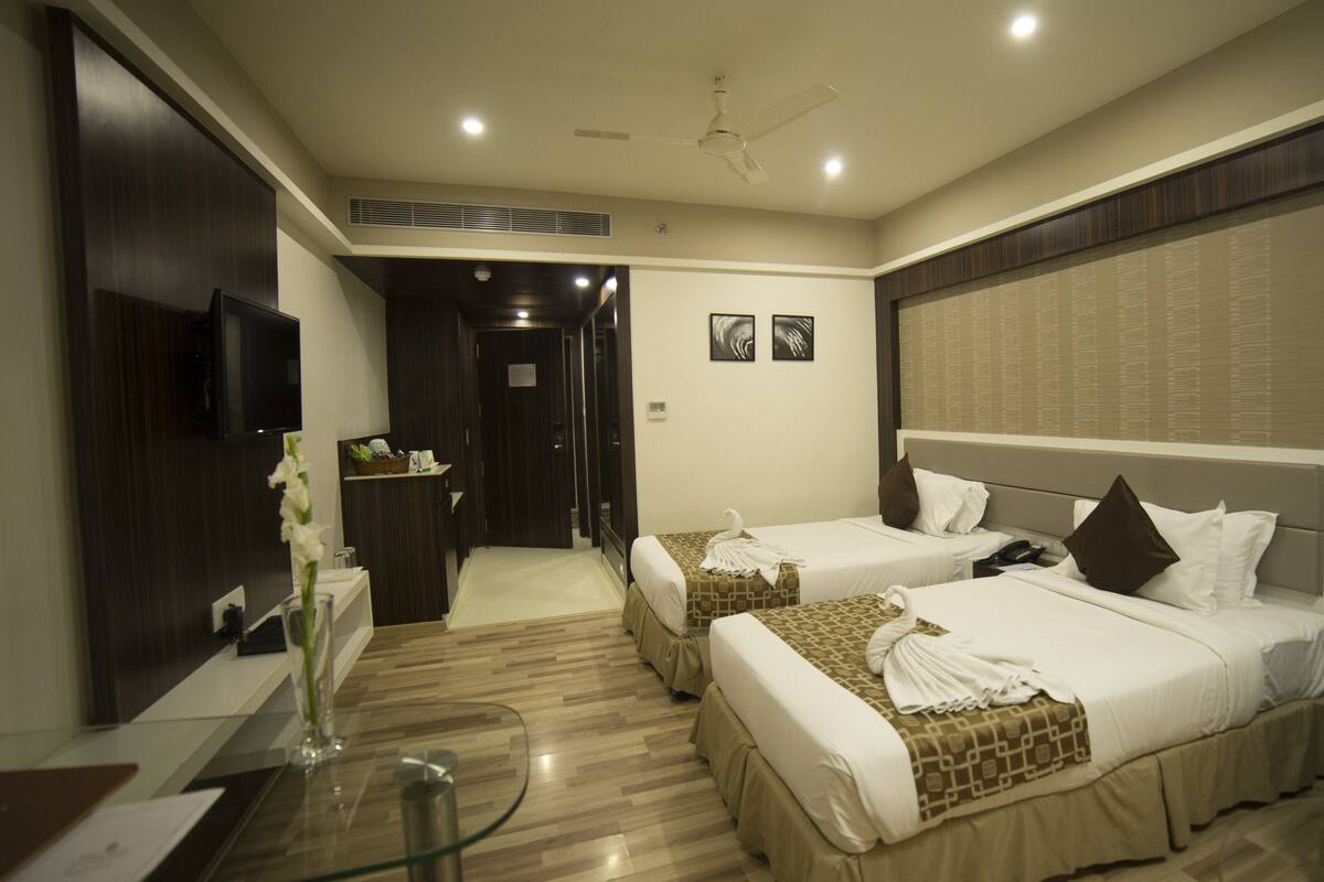Habitación de hotel con dos camas, un escritorio, una silla, un televisor y un ventilador de techo.