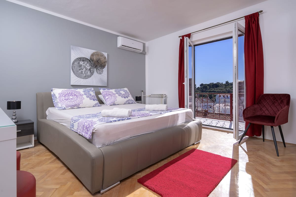 A modern bedroom with a large bed, a red rug, a red chair, and a balcony with red curtains.