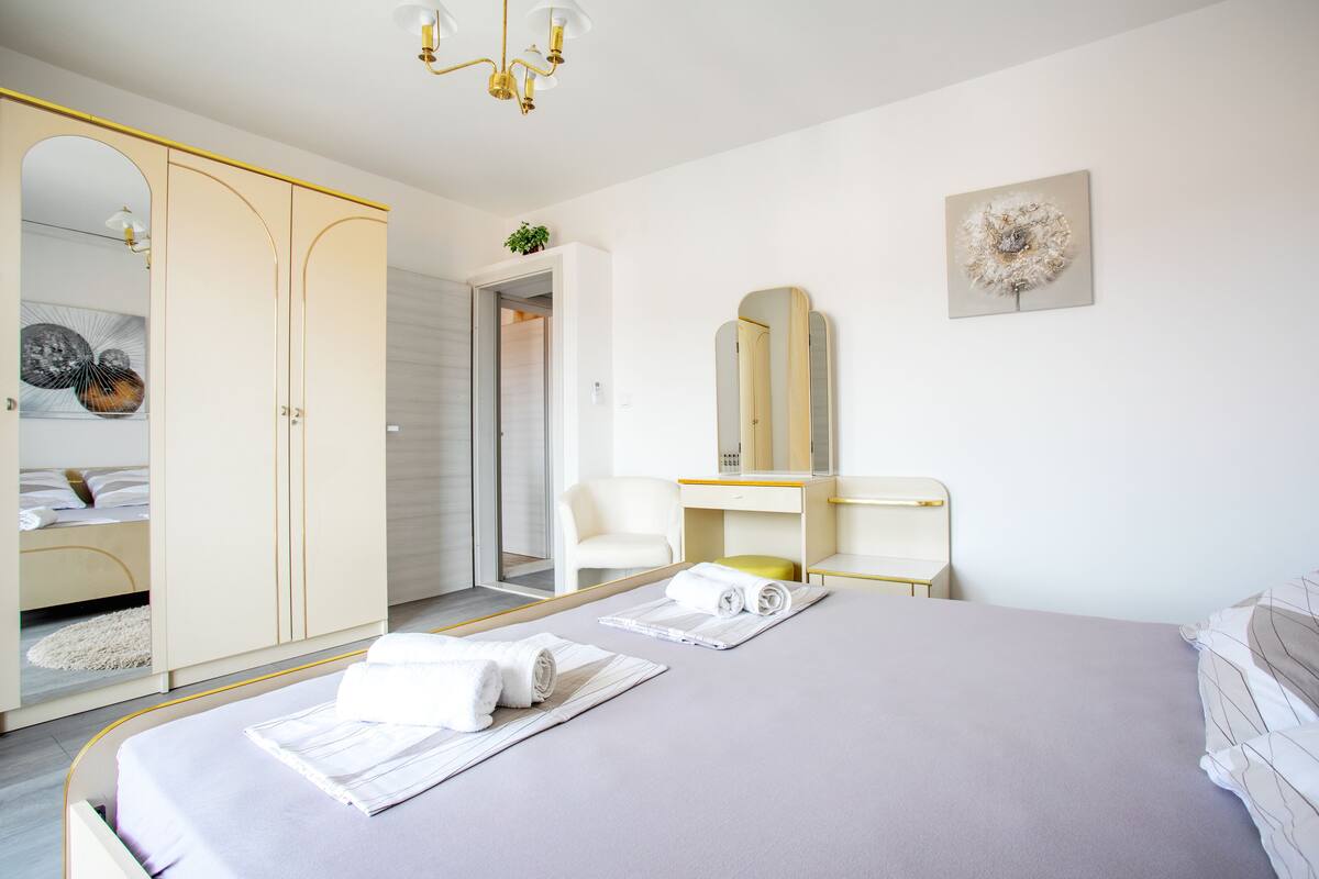 A modern hotel room with a large bed, a desk, a chair, and a wardrobe.