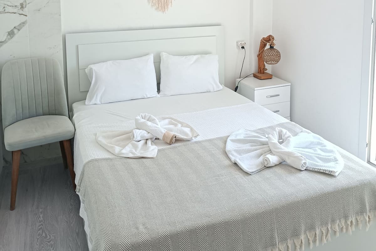 A minimalist bedroom with a bed, bedside table, chair, and a macramé wall hanging.