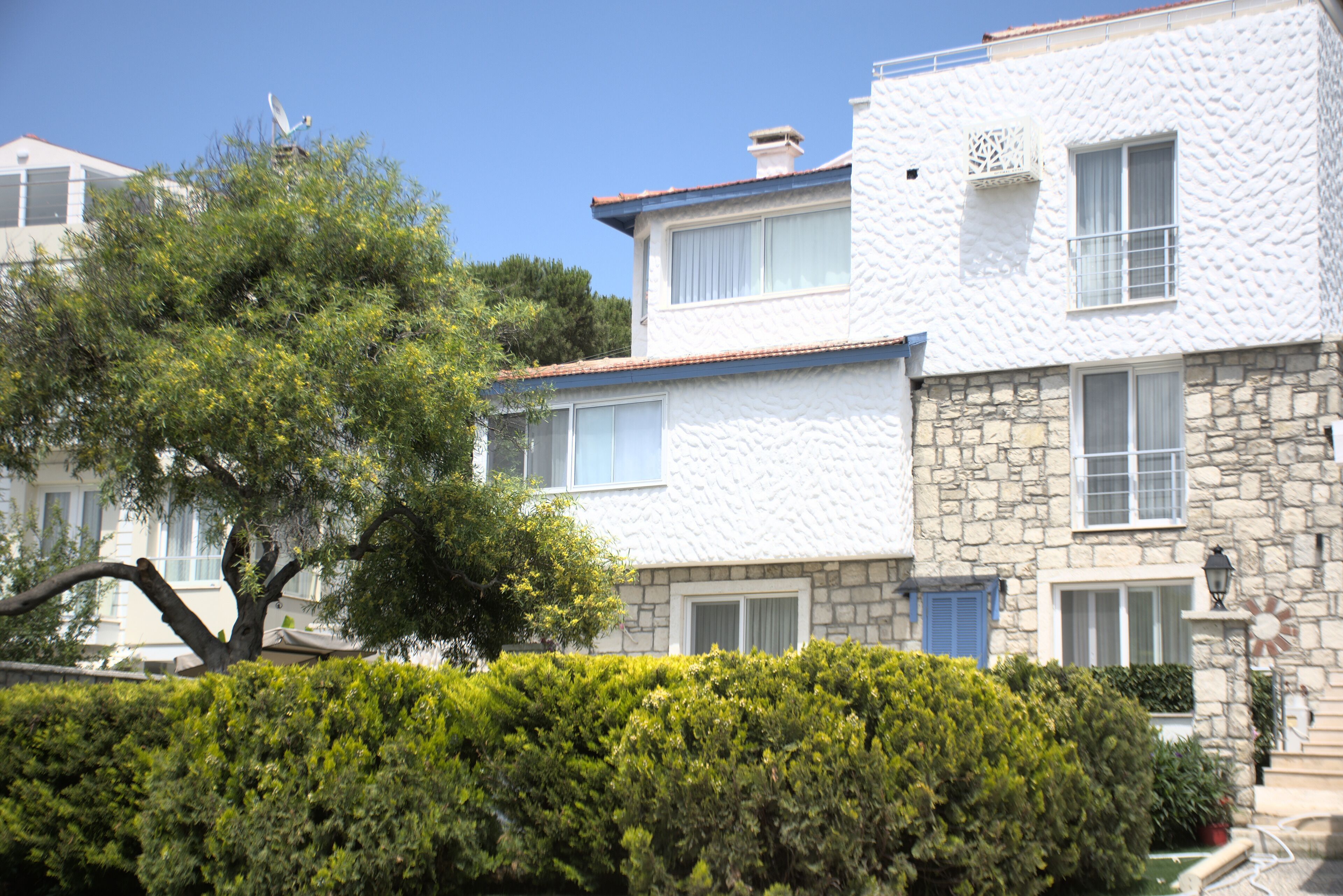 Un edificio de dos pisos con paredes de piedra y textura blanca, varias ventanas y una antena parabólica.