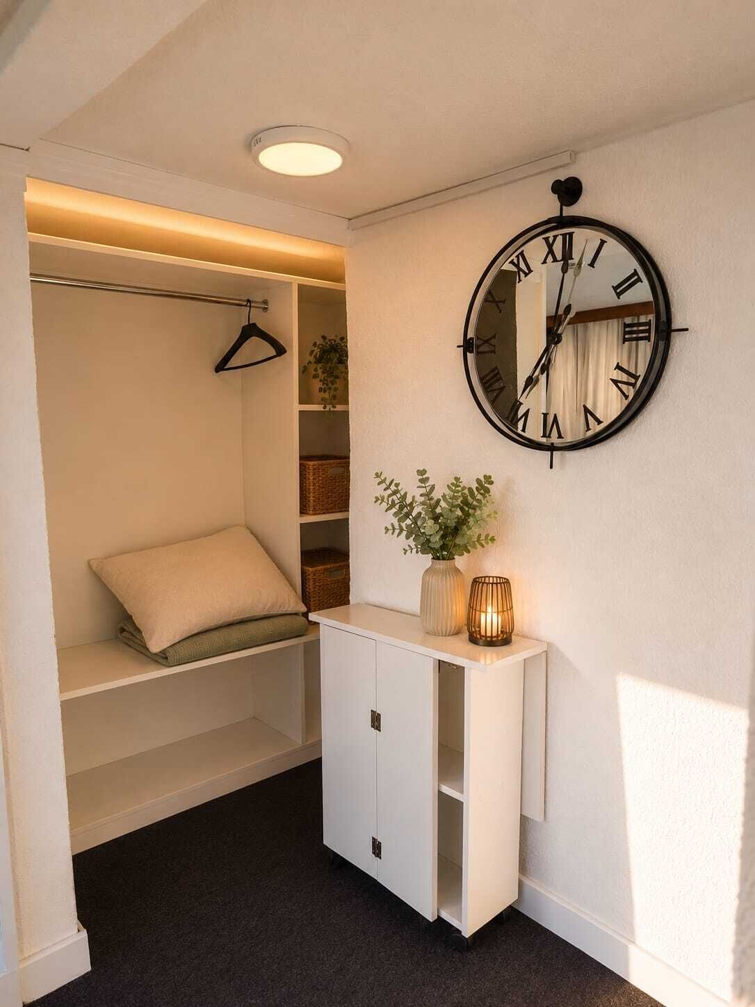 Una habitación con una cama empotrada, un tocador blanco con un reloj y un perchero.
