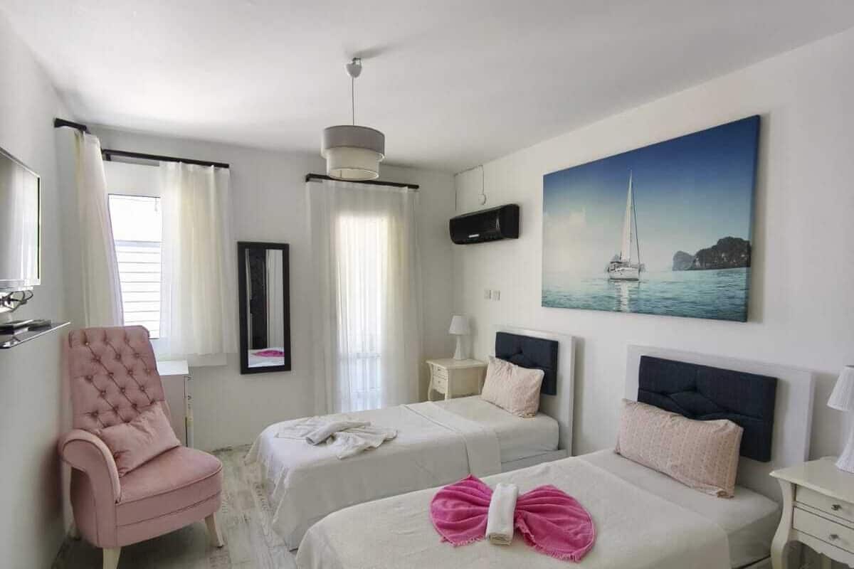 A hotel room with two beds, a chair, a painting of a sailboat, and a ceiling fan.