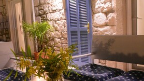 A stone wall interior with a seating area featuring blue upholstered benches and a table with a candle and a potted plant. - Tepe Hotel Alaçatı (Cesme)