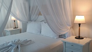 A neatly made bed with white linens and a canopy, a bedside lamp, and a small bedside table with drawers. - Tepe Hotel Alaçatı (Cesme)