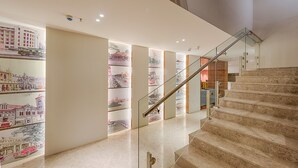 Un interior moderno con una escalera de mármol, barandilla de cristal e ilustraciones de un paisaje urbano en la pared.