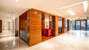 Un vestíbulo espacioso con un mostrador de recepción de madera, una zona de estar roja y vistas despejadas al exterior.