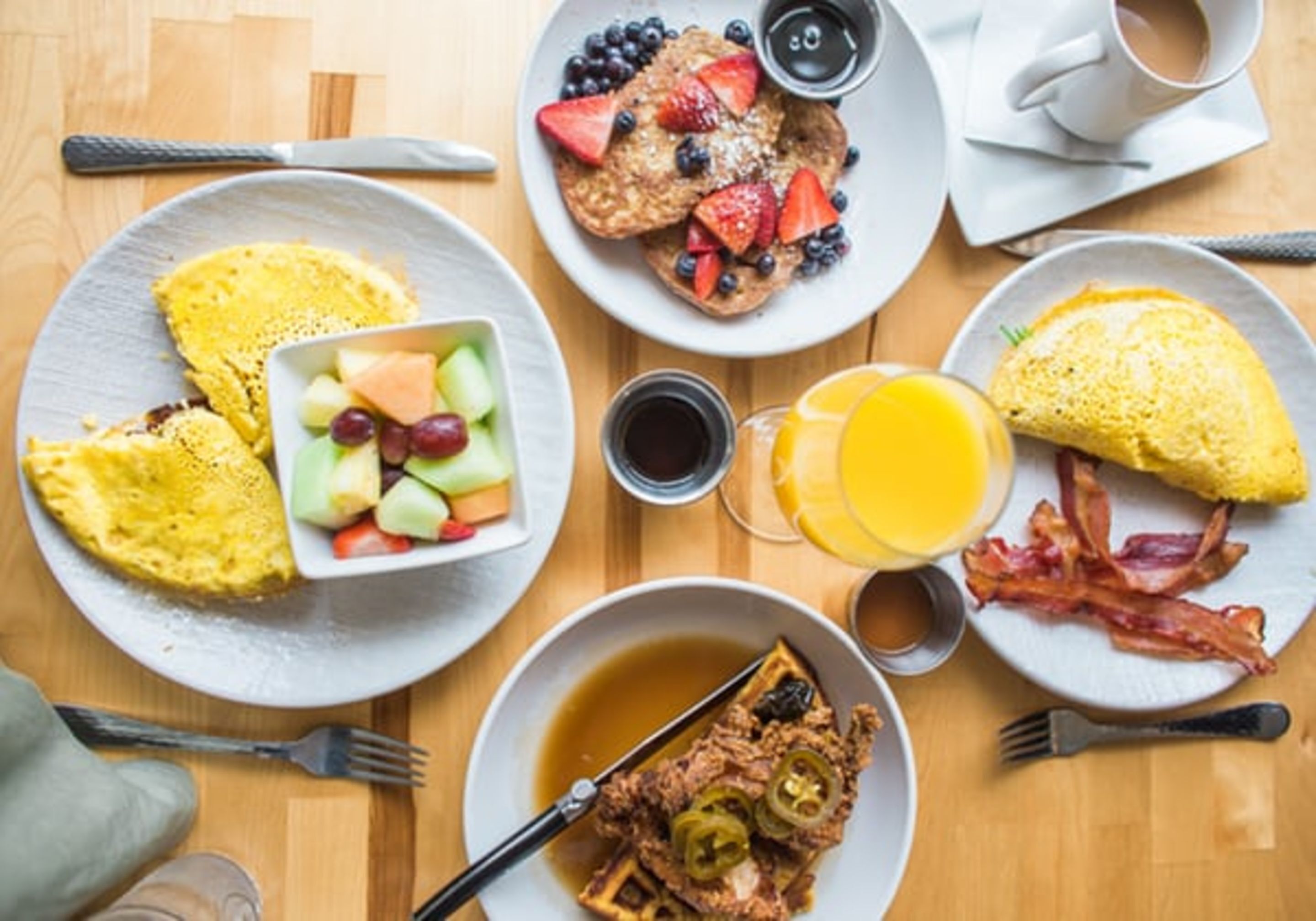 A breakfast setting with various dishes including pancakes, waffles, and eggs, along with a glass of orange juice and a cup of coffee.
