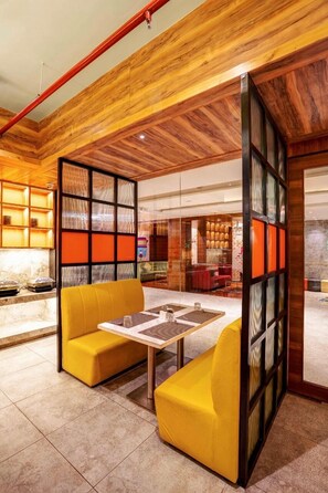 Ein modernes Interieur mit Holzbalken an der Decke, einer gelb gepolsterten Sitzgelegenheit und einem Glastrennfeld mit orangefarbenen Paneelen.