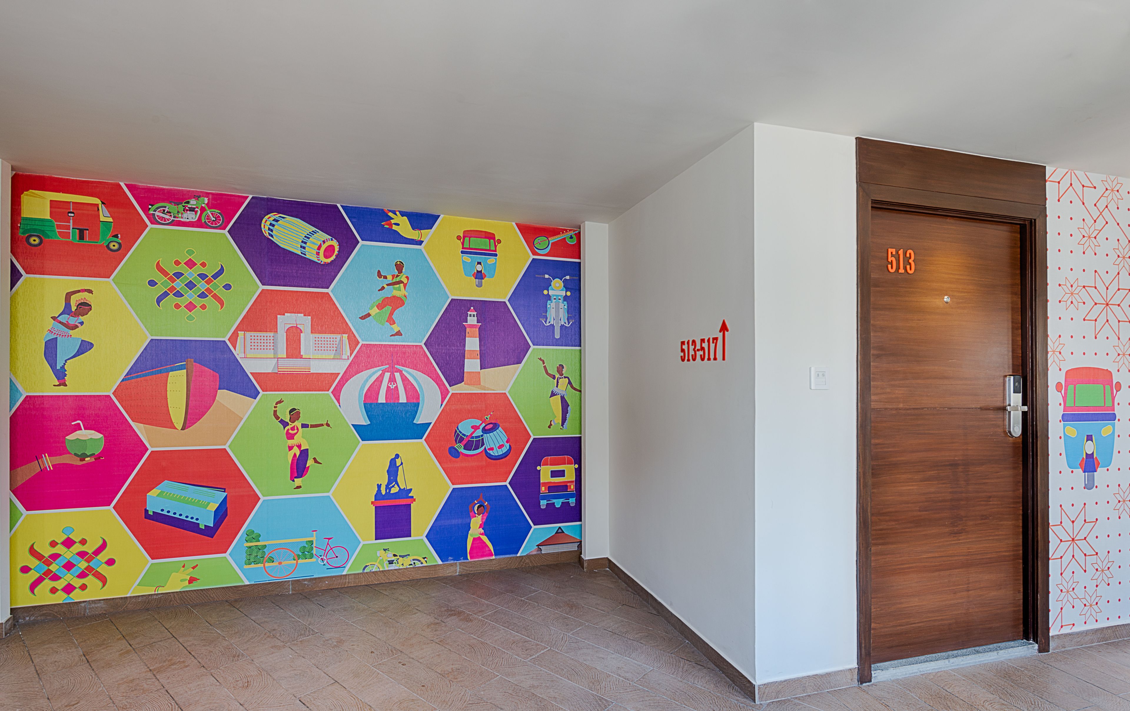 Un pasillo con un revestimiento mural de patrón hexagonal colorido, una puerta de madera con la etiqueta 513, y una pared blanca con un letrero con número de puerta.
