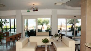 Um hall moderno com sofás brancos, uma mesa de centro e uma área de refeições com cadeiras de vime.