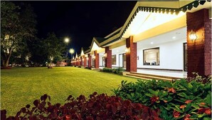 A row of hotel rooms with a well-maintained lawn and flower beds in the foreground. - Trance Greenfields Resort and Convention Centre (Hyderabad)