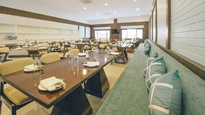 A conference room with multiple tables and chairs, a long sofa with cushions, and a large window providing natural light. - Trance Greenfields Resort and Convention Centre (Hyderabad)