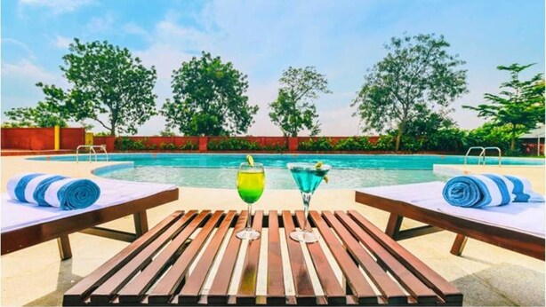 A poolside area with lounge chairs and a table, two drinks, and a clear view of the pool. - Trance Greenfields Resort and Convention Centre (Hyderabad)