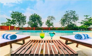 Un área junto a la piscina con sillones de descanso y una mesa, dos bebidas y una vista despejada de la piscina.