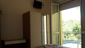 A bedroom with a bed, a wardrobe, a television, and a balcony with a view of greenery.
