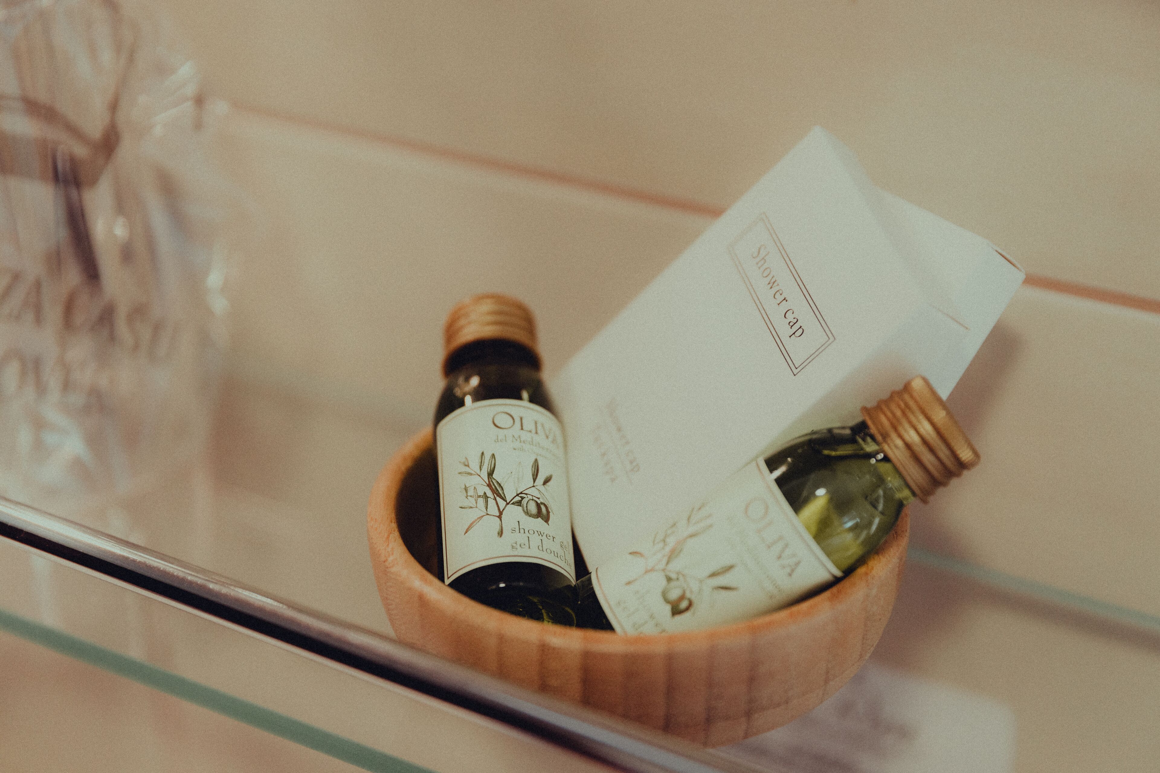 A wooden bowl containing two bottles of olive oil and a white card with text.