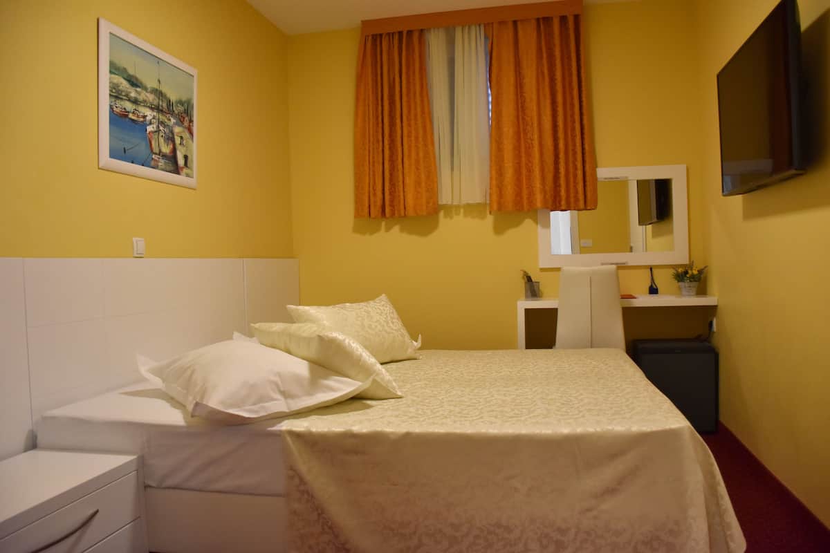 A hotel room with a bed, a bedside table, a small desk, a mirror, and a TV.