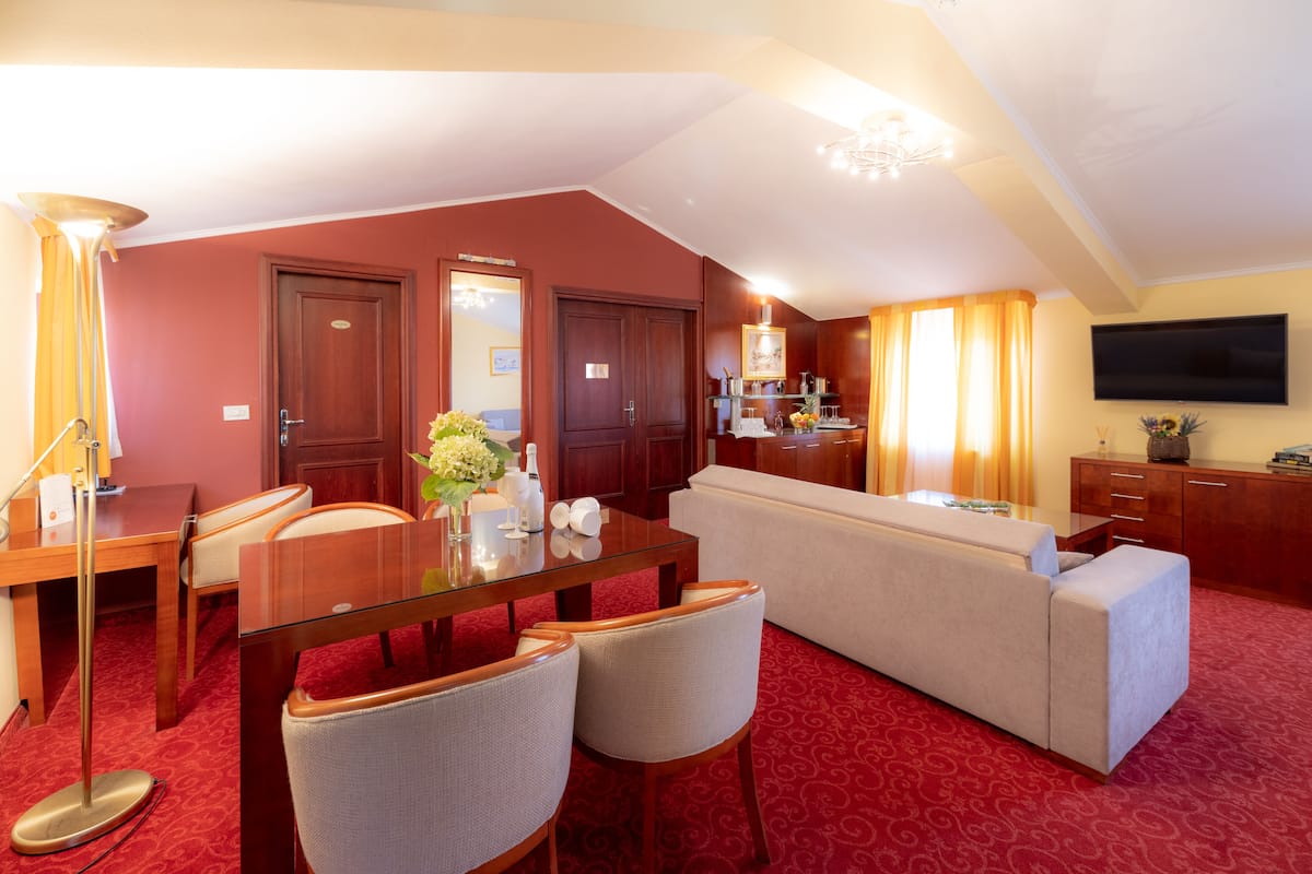 A hotel room with a dining area, a sofa, a TV, and a wooden cabinet.