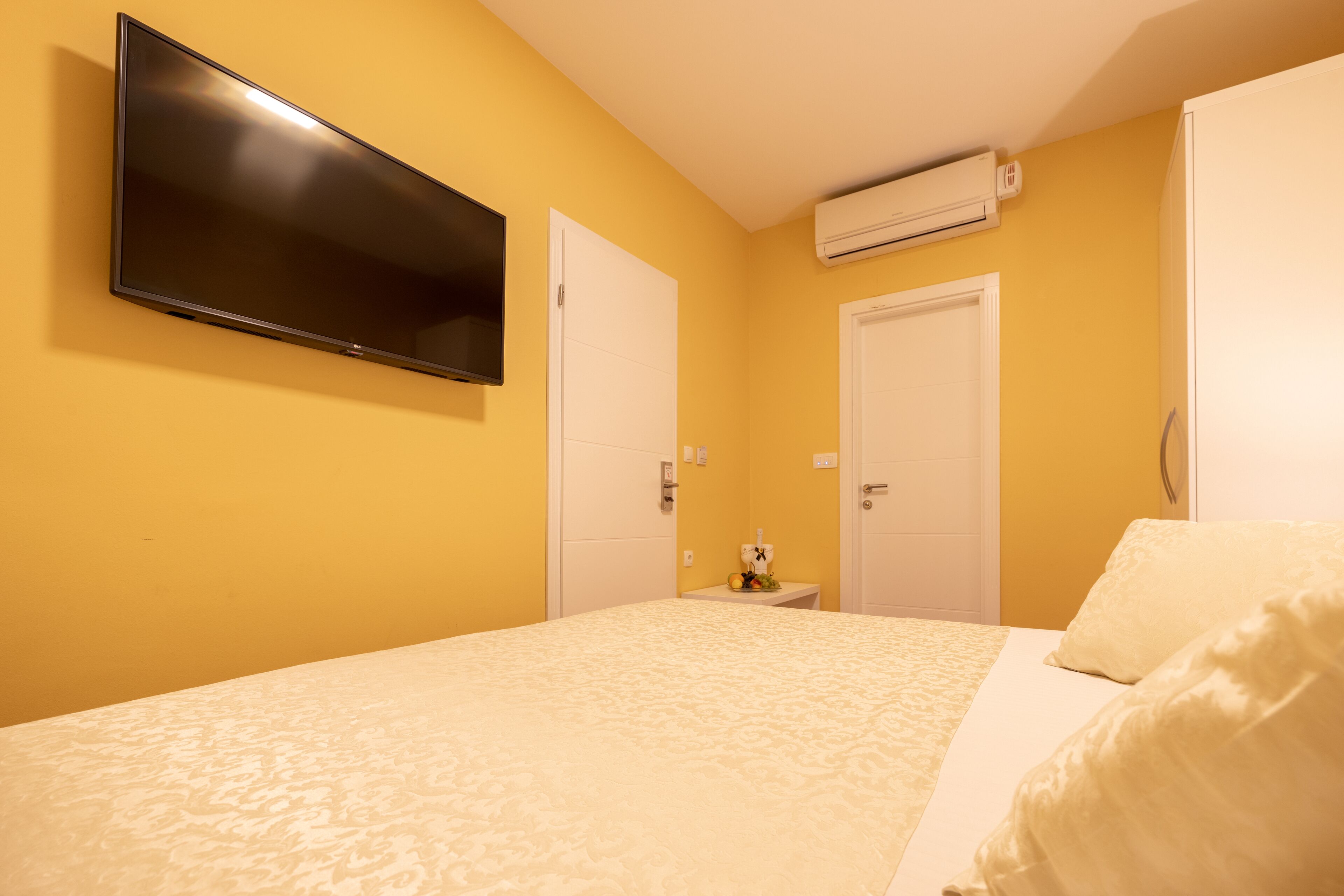 A hotel room with a large bed, a flat-screen TV mounted on the wall, and an air conditioning unit above the door.