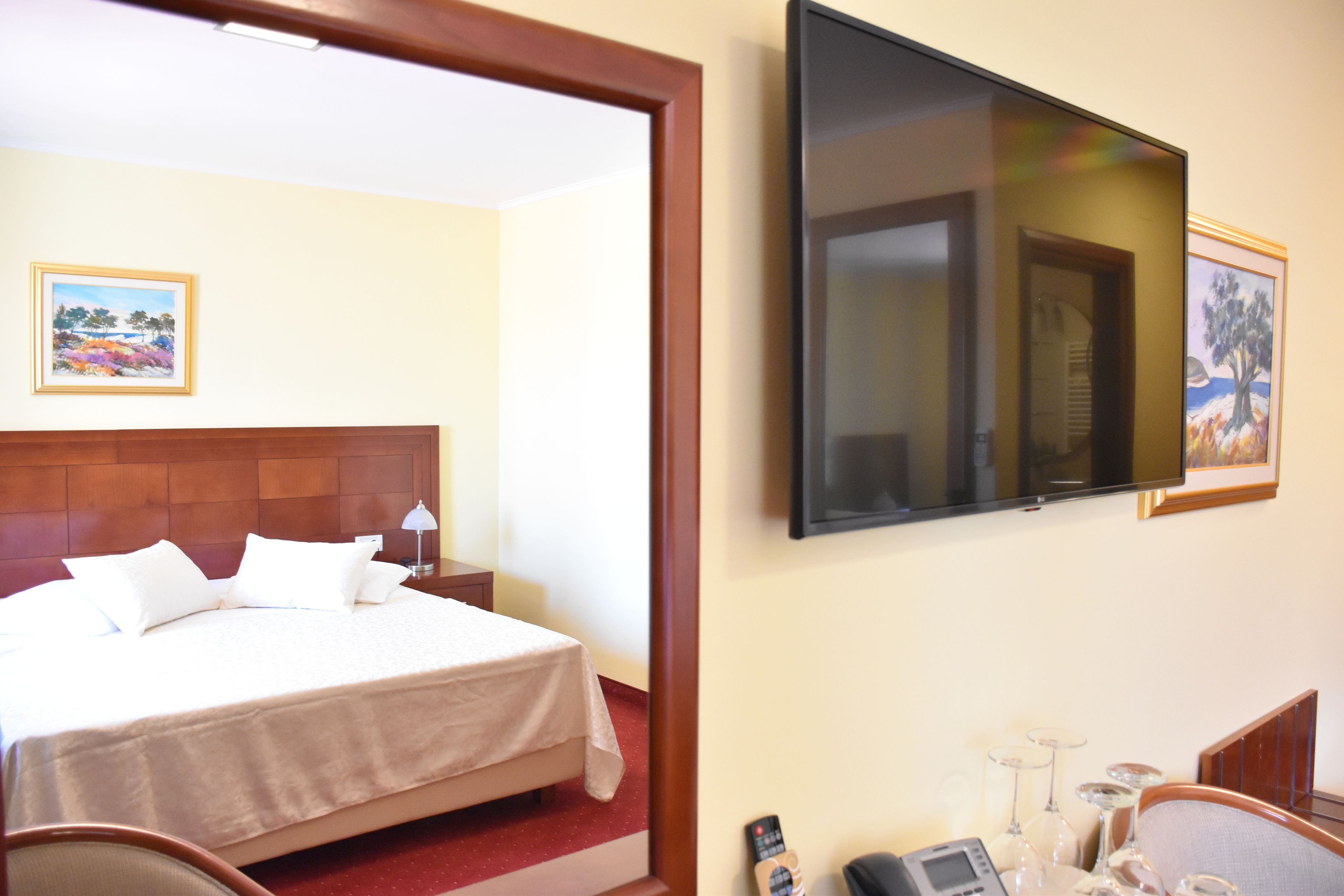 A hotel room with a bed, a TV mounted on the wall, and a desk with a telephone and glasses.