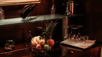 Una zona de bar con un bol de frutas, copas de vino y una botella de vino sobre una encimera de madera oscura.