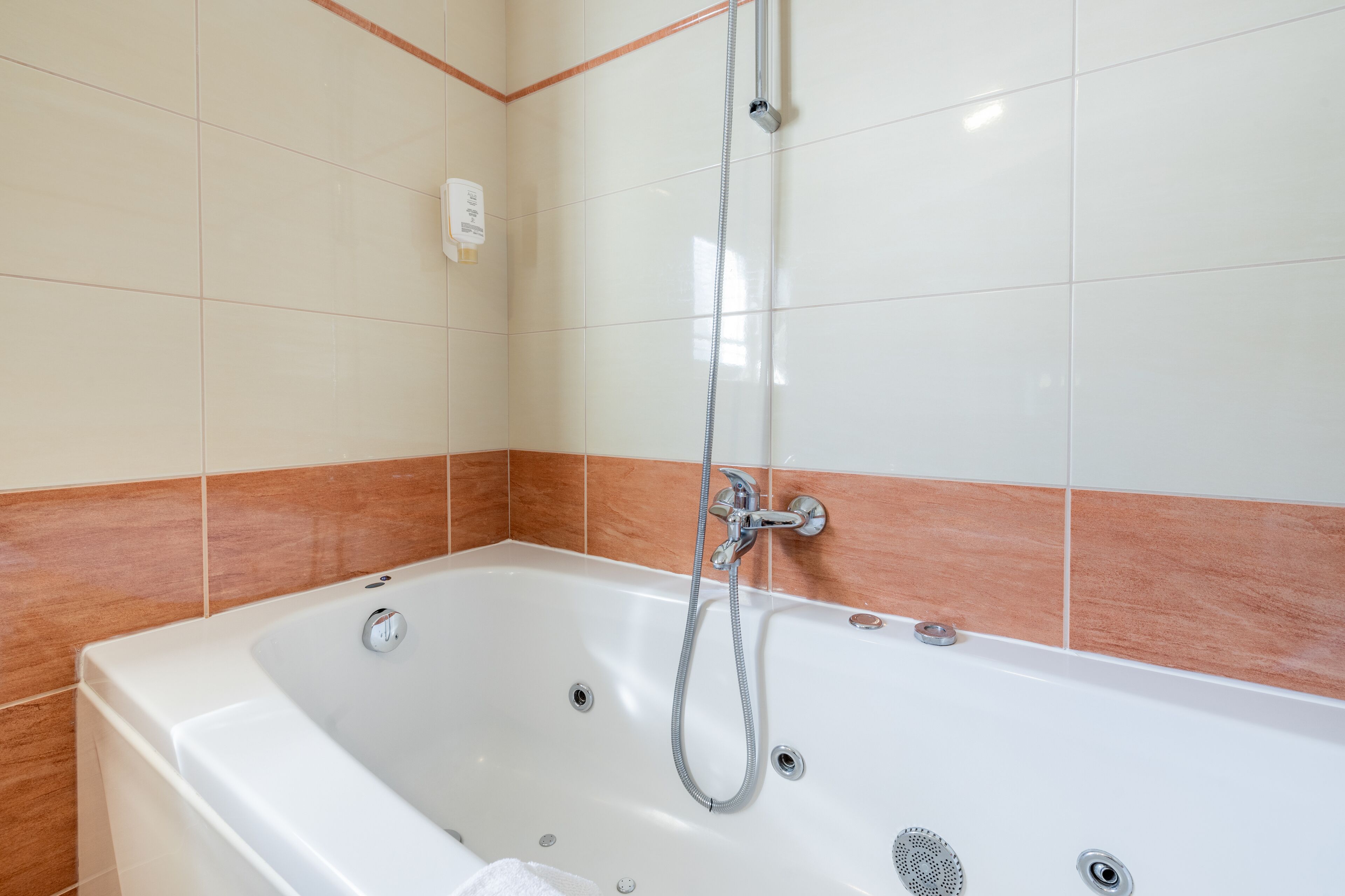 A modern bathroom with a white bathtub, a handheld showerhead, and a corner sink.