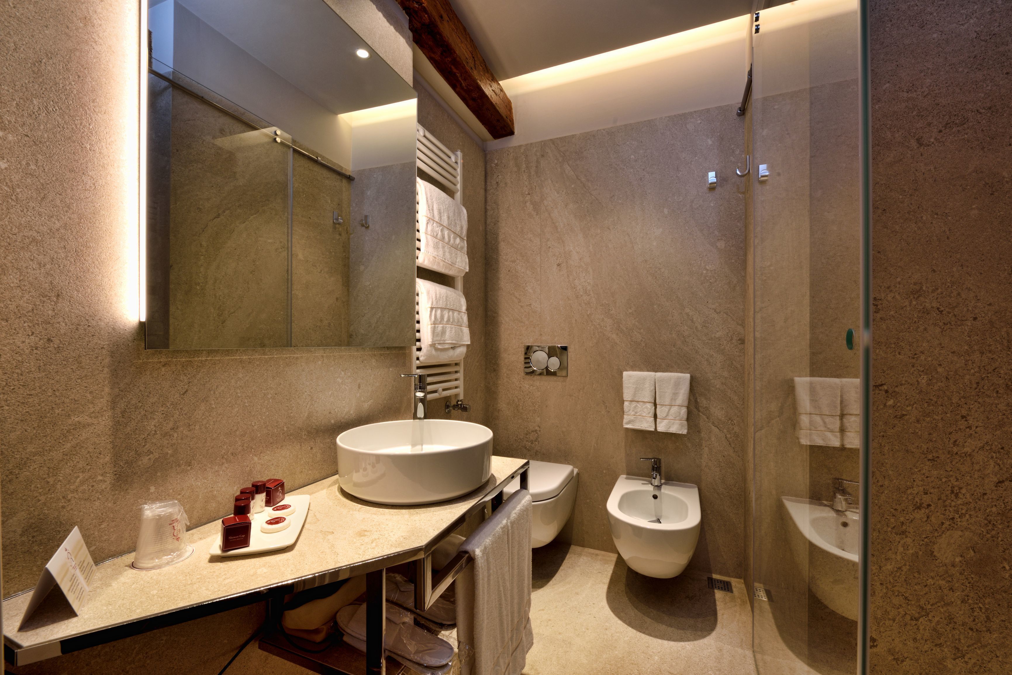 A modern bathroom with a large mirror, a round sink, a bidet, and a glass shower enclosure.