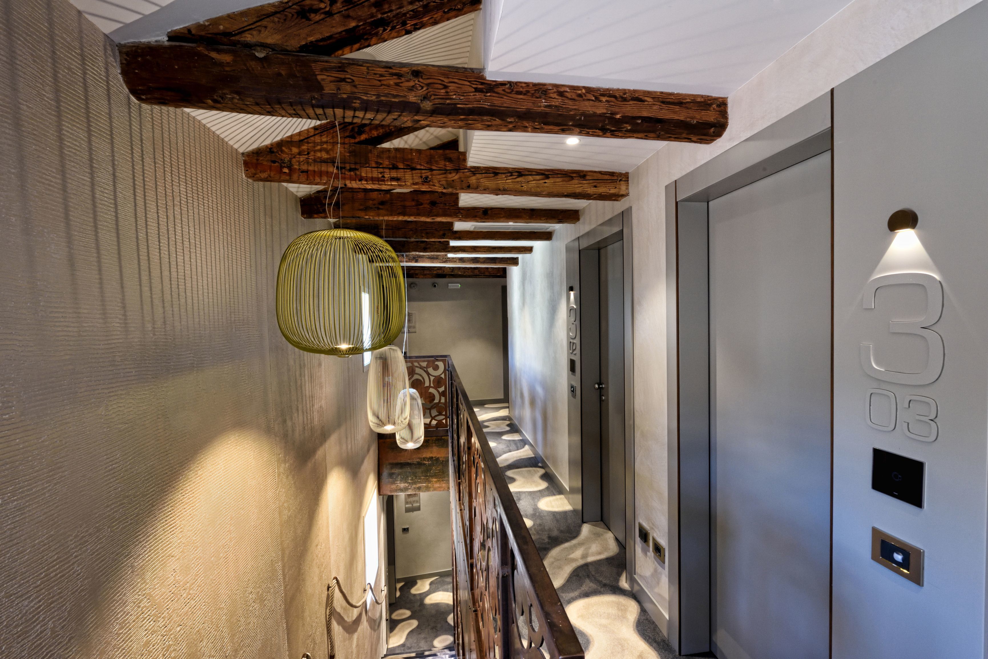 A hallway with a patterned floor, wooden beams, a hanging light fixture, and a door with a number.