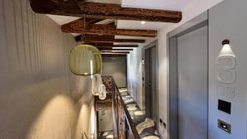 A hallway with a patterned floor, wooden beams, a hanging light fixture, and a door with a number.