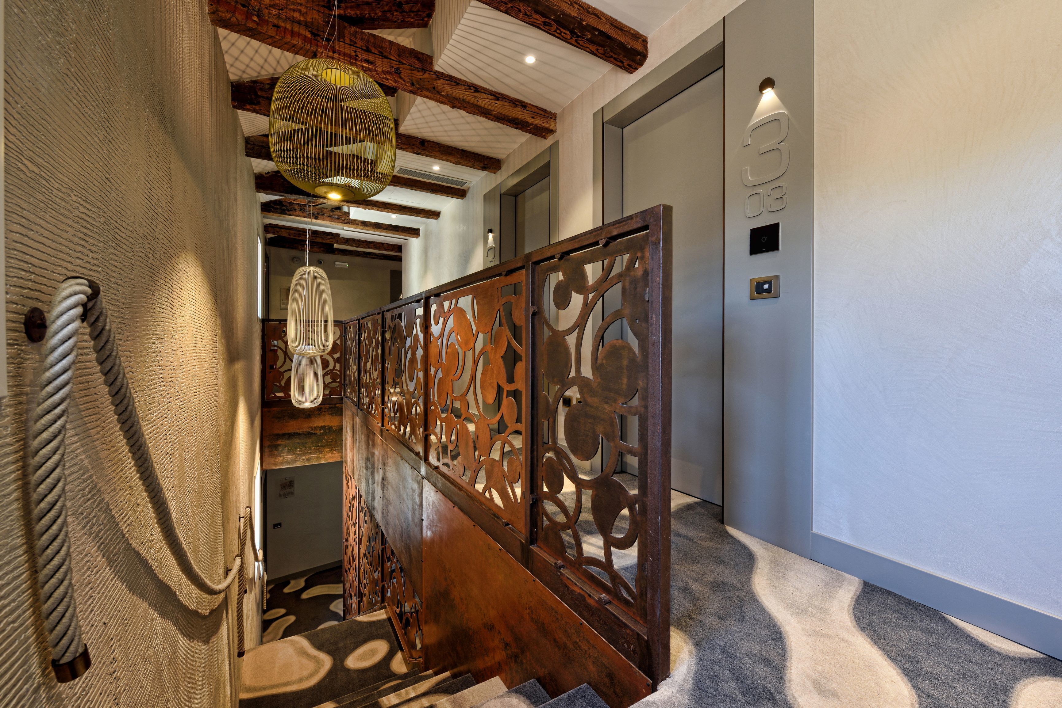 A staircase with a wooden handrail and decorative metal railings, leading to a room with a light switch and a number '3' sign on the wall.