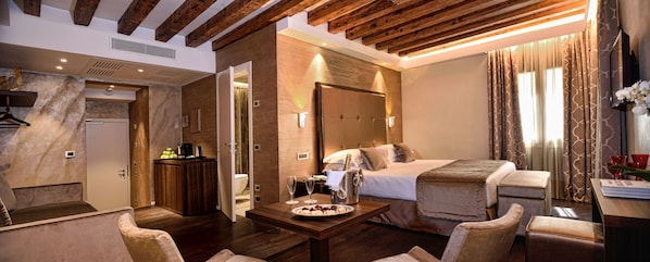 A modern hotel room with a wooden ceiling, a large bed, a sitting area with a table, and a bathroom visible through an open door.
