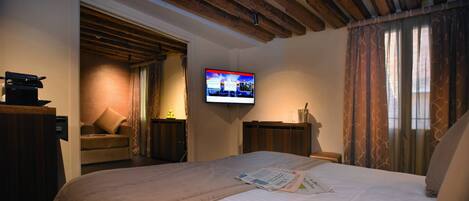 Quarto de hotel com cama, televisão fixada na parede, teto de madeira e janela com cortinas.